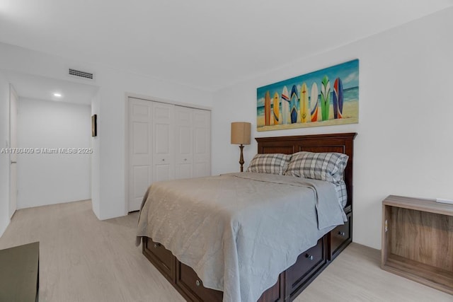bedroom with visible vents, light wood-style flooring, and a closet