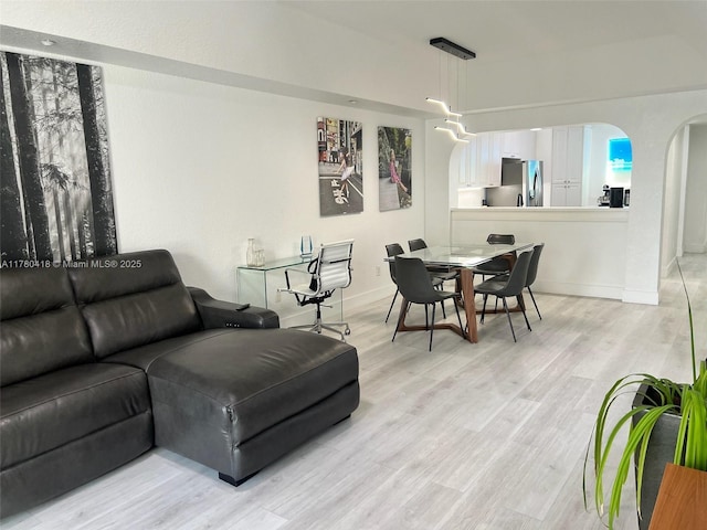 living room with arched walkways, light wood finished floors, and baseboards