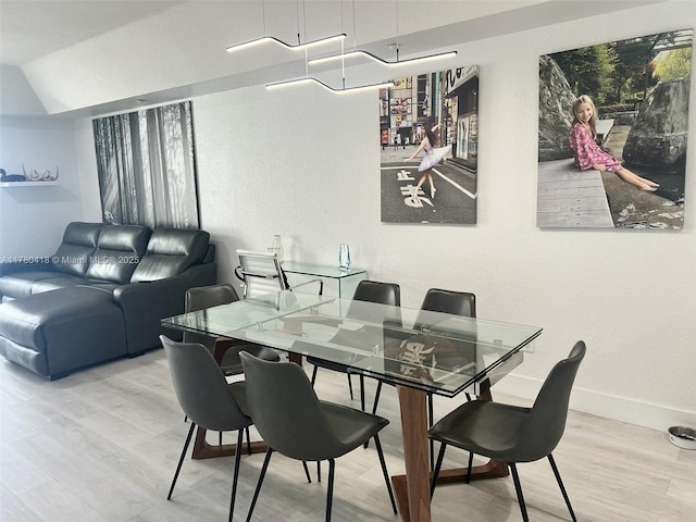 dining area featuring a textured wall, lofted ceiling, baseboards, and wood finished floors