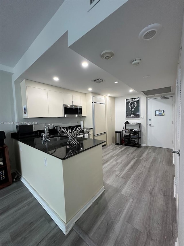 kitchen featuring visible vents, stainless steel microwave, a sink, dark countertops, and paneled built in refrigerator
