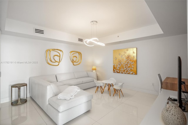 tiled living area featuring a notable chandelier, visible vents, baseboards, and a tray ceiling