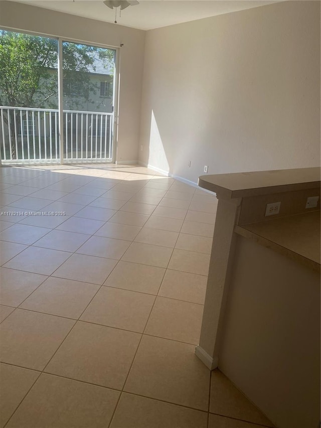 tiled empty room featuring baseboards and ceiling fan
