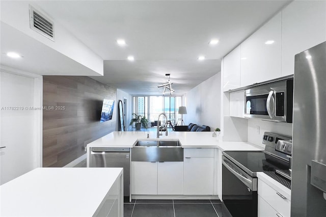 kitchen featuring visible vents, an accent wall, a sink, appliances with stainless steel finishes, and a peninsula