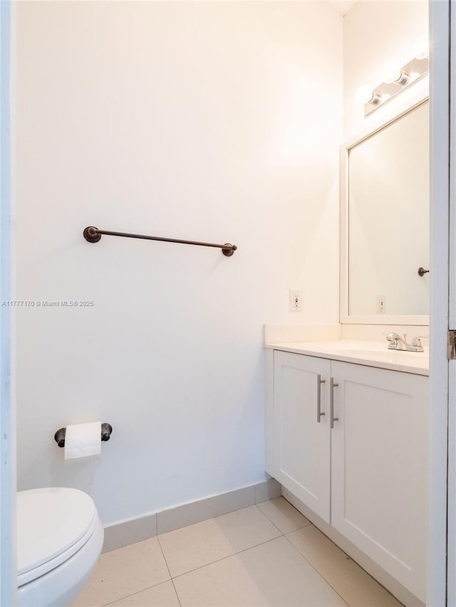 half bathroom with toilet, tile patterned floors, vanity, and baseboards