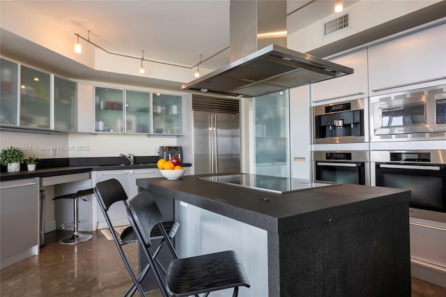 kitchen featuring visible vents, built in appliances, dark countertops, island exhaust hood, and a sink