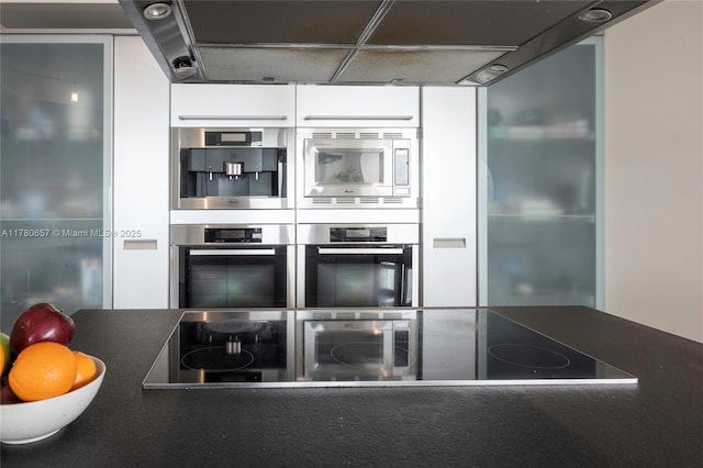 kitchen with white cabinets, stainless steel appliances, dark countertops, and under cabinet range hood