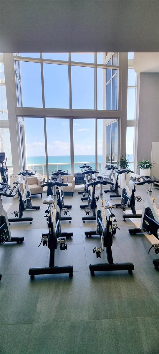 workout area featuring floor to ceiling windows, a water view, and a high ceiling