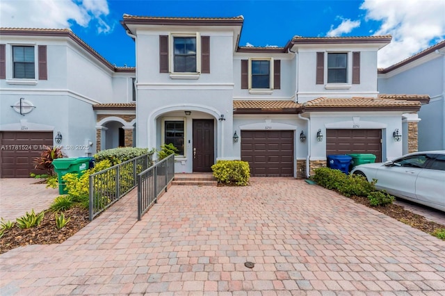 mediterranean / spanish home featuring stucco siding, stone siding, decorative driveway, a garage, and a tiled roof