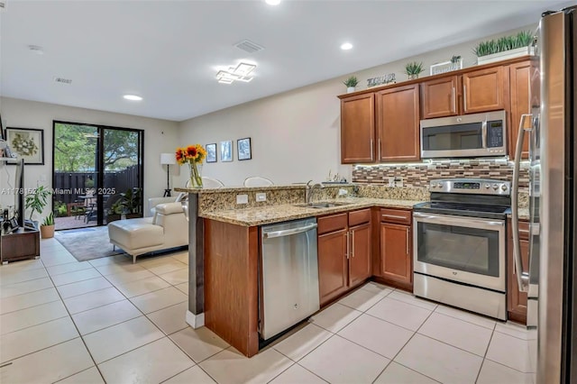 kitchen with a sink, open floor plan, a peninsula, brown cabinetry, and stainless steel appliances