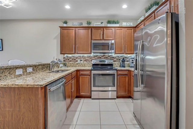 kitchen featuring light stone counters, a peninsula, brown cabinets, stainless steel appliances, and a sink