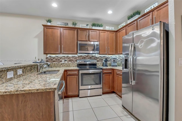 kitchen with light tile patterned floors, light stone countertops, a sink, stainless steel appliances, and brown cabinets