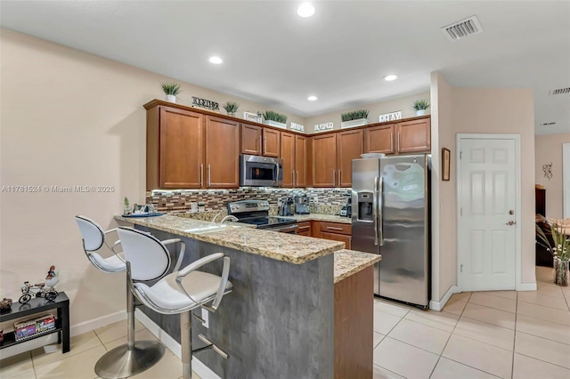 kitchen with light stone counters, a peninsula, visible vents, brown cabinets, and appliances with stainless steel finishes