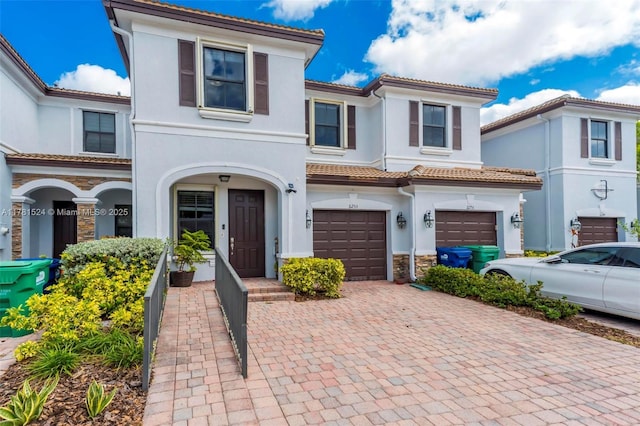 mediterranean / spanish-style house with a garage, stucco siding, stone siding, and decorative driveway