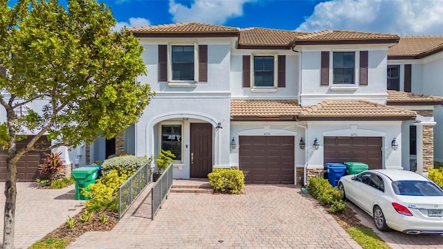 mediterranean / spanish-style house with a tiled roof, decorative driveway, a garage, and stucco siding