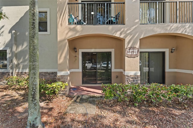 entrance to property with stone siding, a balcony, and stucco siding
