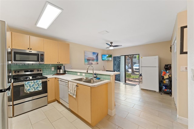 kitchen with a peninsula, a sink, decorative backsplash, light brown cabinets, and appliances with stainless steel finishes
