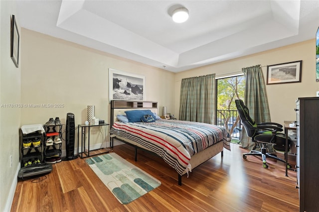 bedroom with access to exterior, wood finished floors, and a raised ceiling