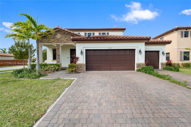 mediterranean / spanish house with a tiled roof, an attached garage, stone siding, stucco siding, and decorative driveway