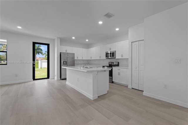 kitchen with white cabinets, light countertops, an island with sink, stainless steel appliances, and light wood-style flooring