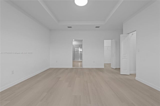 unfurnished bedroom with a spacious closet, light wood-style flooring, visible vents, and a raised ceiling