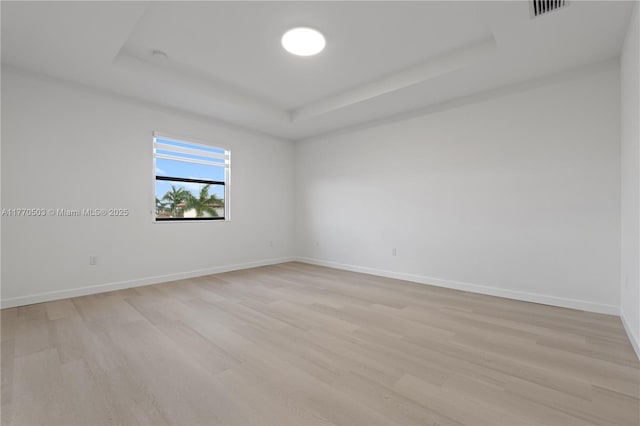 unfurnished room featuring visible vents, light wood-style flooring, a raised ceiling, and baseboards
