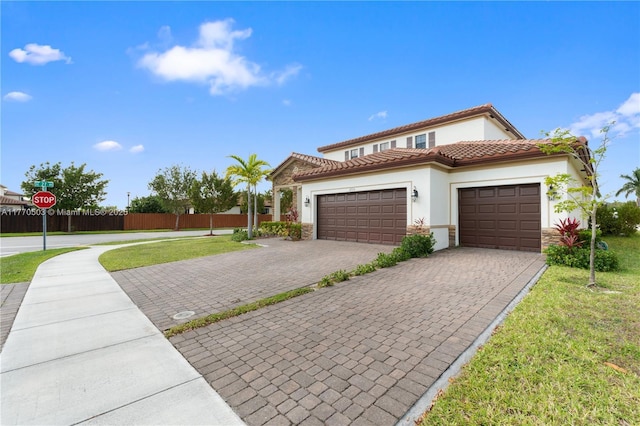 mediterranean / spanish-style home featuring decorative driveway, a front yard, stone siding, fence, and a garage