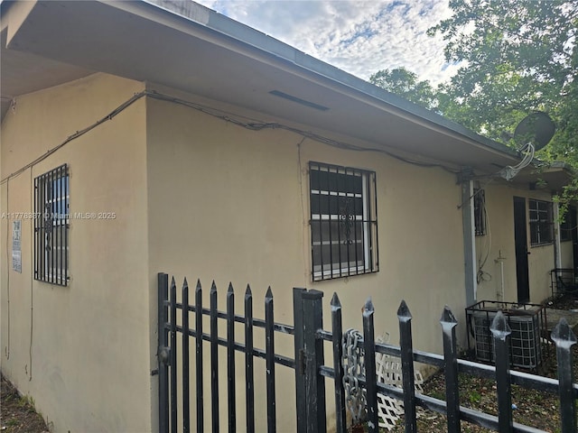view of side of home featuring central AC, fence, and stucco siding