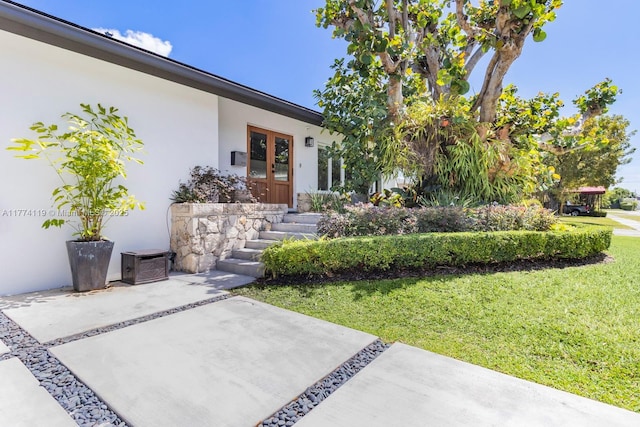 doorway to property featuring a patio, french doors, stucco siding, and a yard
