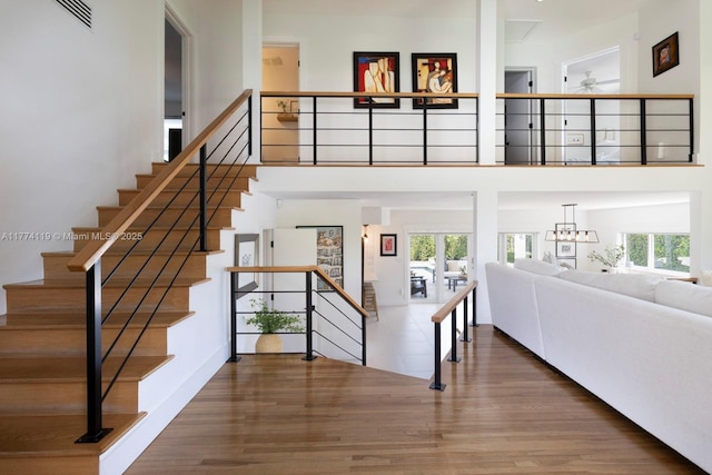 stairway with ceiling fan, visible vents, a high ceiling, and wood finished floors