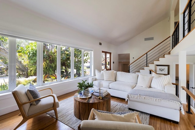 living area featuring stairway, visible vents, vaulted ceiling, and wood finished floors