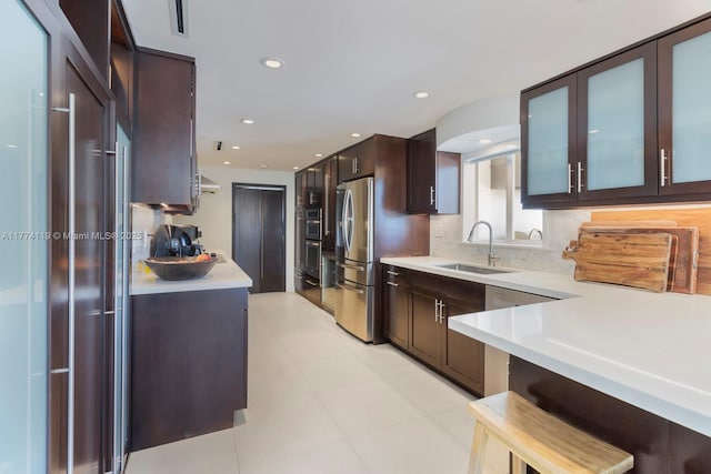 kitchen with tasteful backsplash, glass insert cabinets, light countertops, dark brown cabinets, and a sink