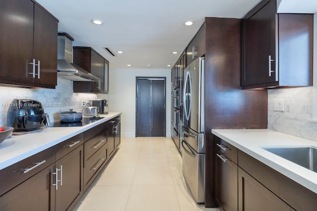 kitchen with wall chimney exhaust hood, dark brown cabinets, appliances with stainless steel finishes, light countertops, and decorative backsplash