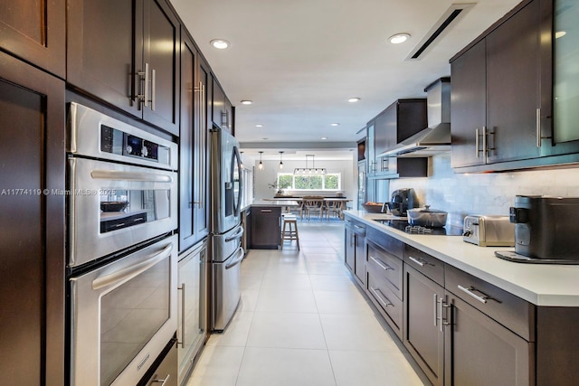 kitchen featuring wall chimney exhaust hood, light tile patterned flooring, light countertops, stainless steel appliances, and backsplash