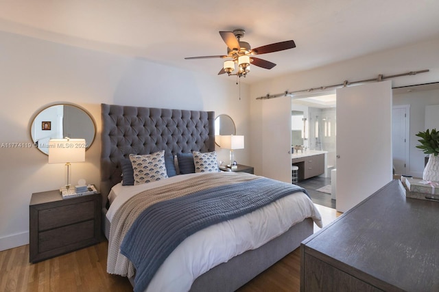 bedroom with ensuite bathroom, a ceiling fan, a barn door, and wood finished floors