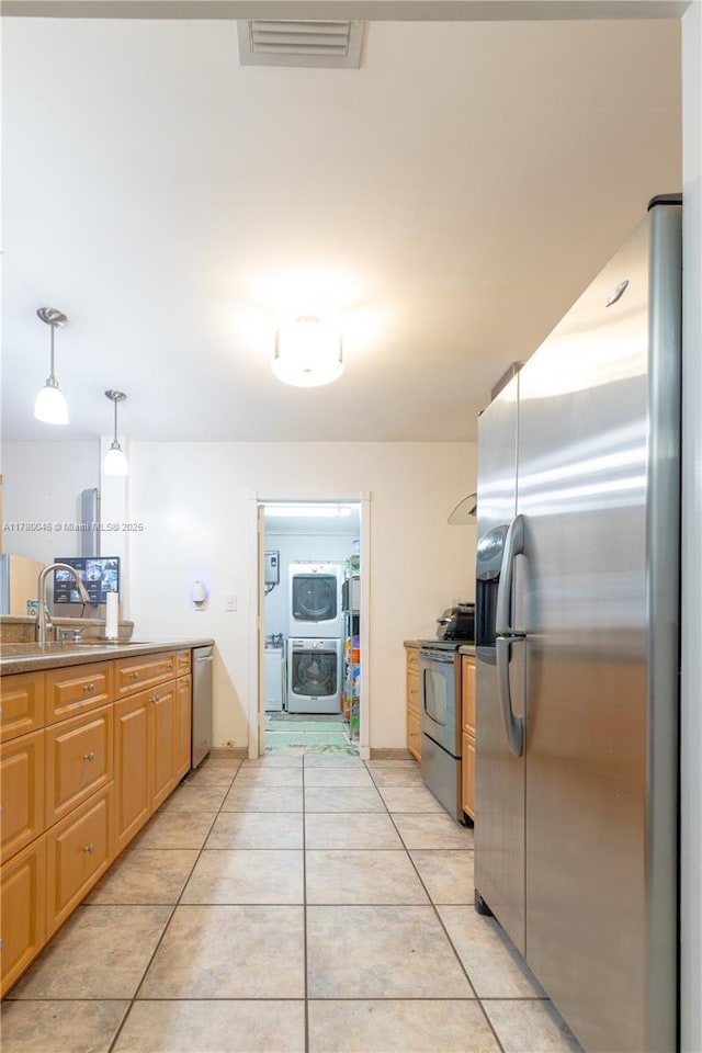 kitchen with stainless steel appliances, light tile patterned floors, washer / dryer, decorative light fixtures, and a sink
