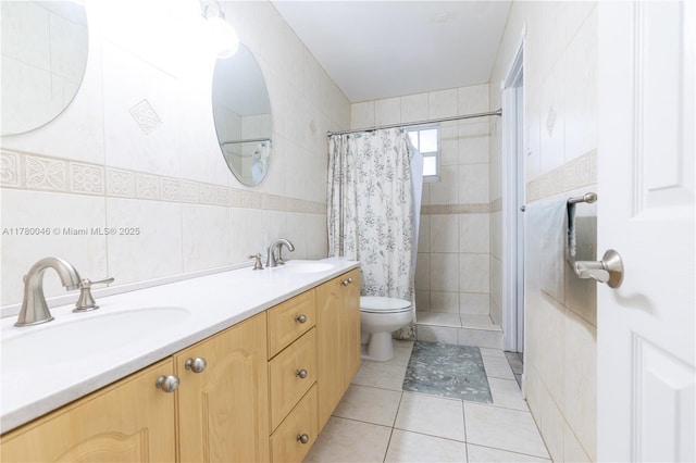 full bathroom featuring toilet, tile patterned flooring, a tile shower, double vanity, and tile walls