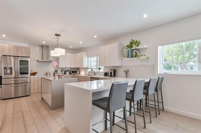 kitchen featuring appliances with stainless steel finishes, light wood finished floors, wall chimney exhaust hood, and modern cabinets