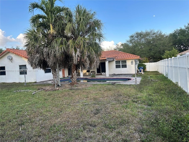 back of property with a fenced in pool, stucco siding, a fenced backyard, a tile roof, and a yard