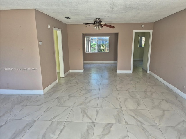 empty room with marble finish floor, baseboards, a ceiling fan, and visible vents