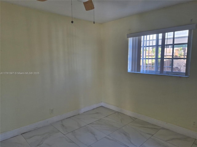 empty room with ceiling fan, marble finish floor, and baseboards