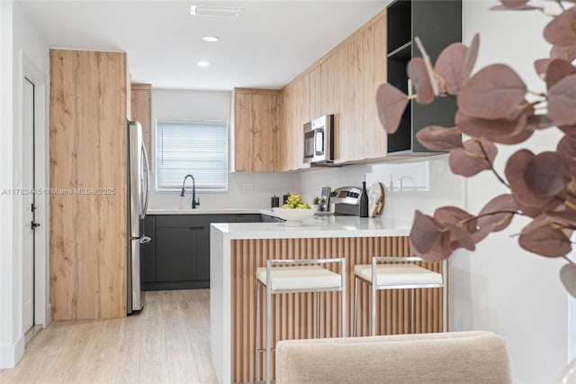 kitchen with light wood-style floors, a peninsula, a breakfast bar, light countertops, and stainless steel appliances