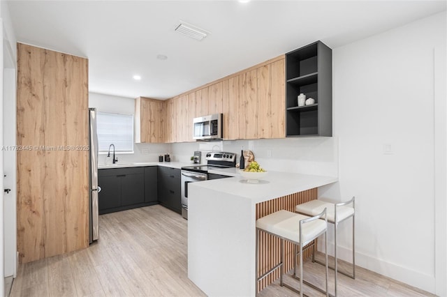 kitchen with a peninsula, light wood-type flooring, open shelves, light countertops, and appliances with stainless steel finishes