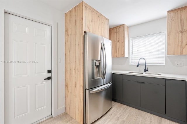 kitchen featuring light wood-style flooring, light countertops, a sink, stainless steel fridge, and gray cabinetry
