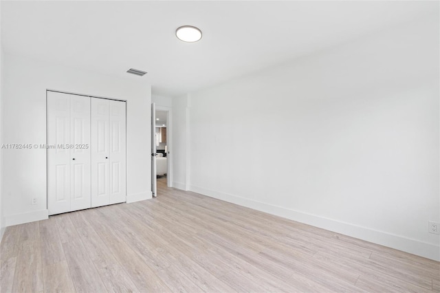 unfurnished bedroom with light wood-style flooring, a closet, baseboards, and visible vents