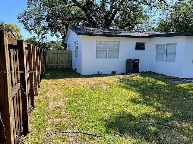 exterior space with a yard, central AC, a fenced backyard, and stucco siding