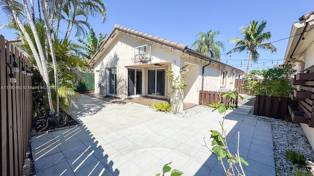 rear view of property featuring a patio area, a tile roof, fence, and stucco siding