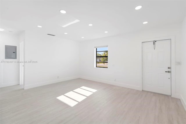 empty room featuring light wood-style flooring, visible vents, electric panel, recessed lighting, and baseboards