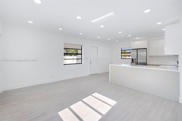 kitchen featuring modern cabinets, white cabinetry, light countertops, stainless steel fridge, and light wood finished floors