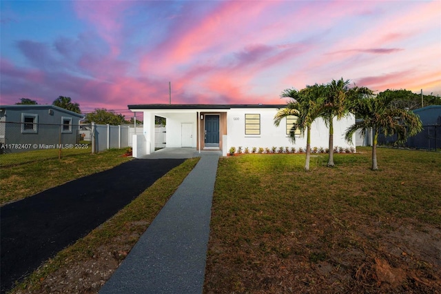 bungalow featuring stucco siding, an attached carport, aphalt driveway, fence, and a lawn