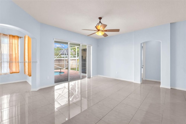 empty room featuring tile patterned flooring, arched walkways, a textured ceiling, a ceiling fan, and baseboards